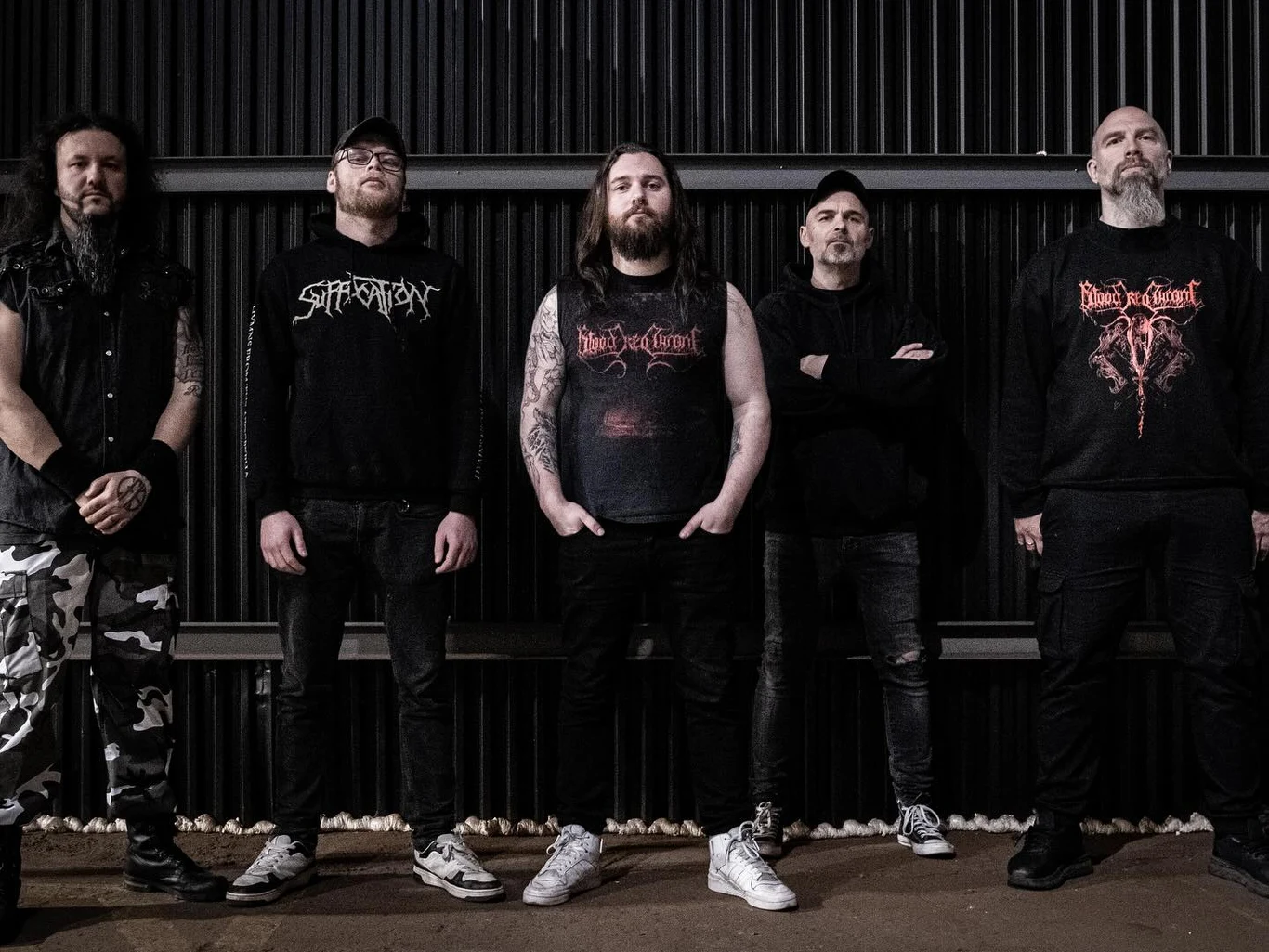 Blood Red Throne szykuje nowy album "Siltskin" Pięciu mężczyzn stojących obok siebie na tle ciemnej, metalowej ściany, ubranych w ciemne ubrania z nadrukami związanymi z muzyką metalową, część z nich ma brody i tatuaże.