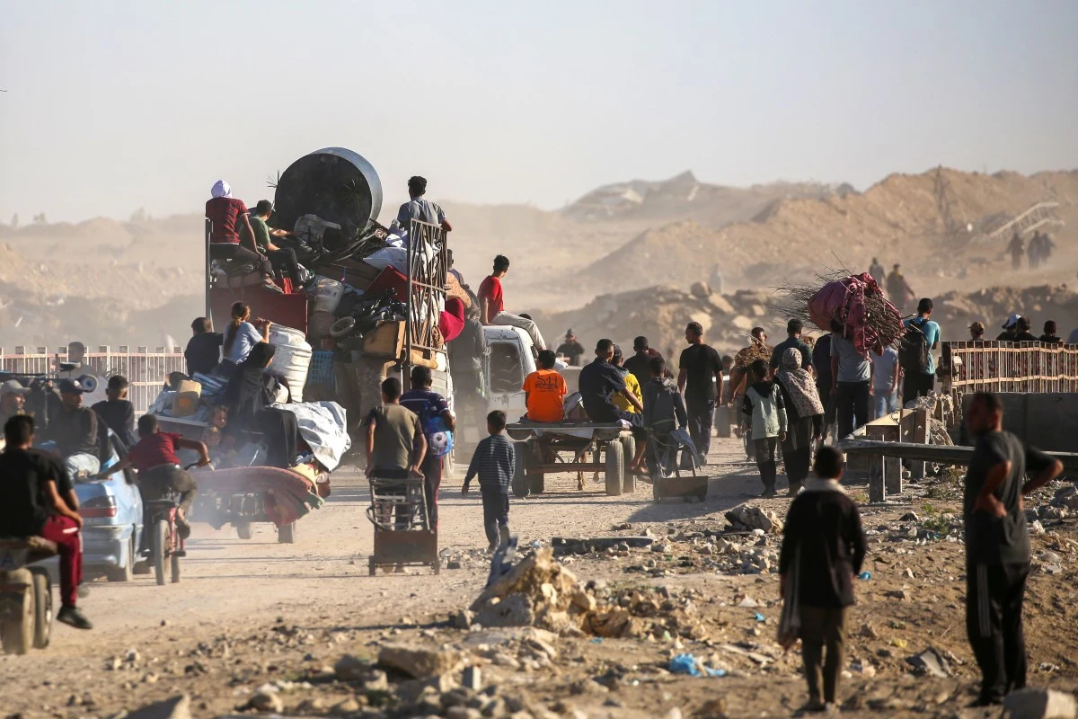 Palestyńczycy idący w stronę Gazy Ludzie przemieszczający się pieszo i na wozach przez zniszczony, piaszczysty teren, część osób niesie swoje rzeczy lub przewozi je w pojazdach, wokół widoczne gruzy i kurz, krajobraz sugeruje trudne warunki i masowy exodus.