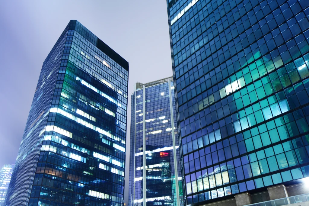 Nowoczesne wieżowce z przeszklonymi fasadami, oświetlone licznymi światłami biurowymi, dominujące nad miejskim krajobrazem nocą.