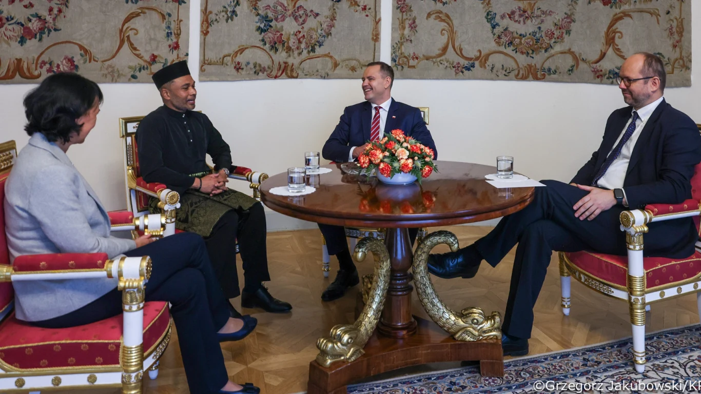 Karol Nawrocki spotkał się z ambasadorami. Uroczystość w Belwederze Cztery osoby siedzą przy okrągłym stole w elegancko urządzonym pomieszczeniu, prowadząc oficjalną rozmowę; na stole stoi ozdobna kompozycja kwiatowa i szklanki z wodą, w tle widoczne są gobeliny na ścianach.