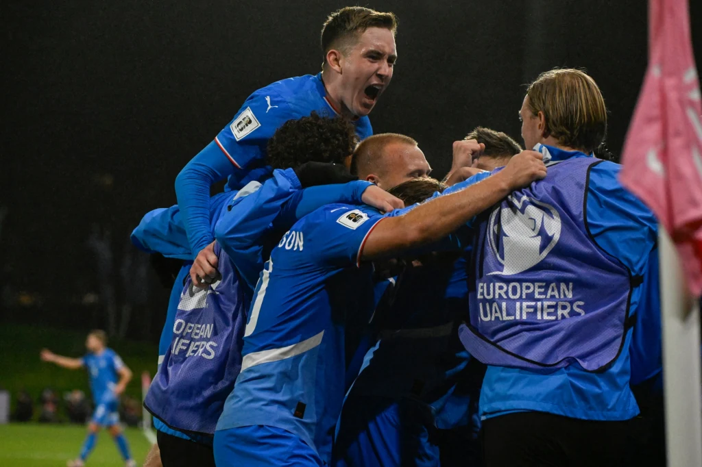 Radość Islandczyków po drugiej bramce, która dała im punkt w starciu z aktualnymi wicemistrzami świata Grupa piłkarzy w niebieskich strojach celebruje zdobycie bramki, zawodnicy obejmują się i krzyczą z radości, atmosfera pełna emocji, w tle widoczny ciemny stadion.