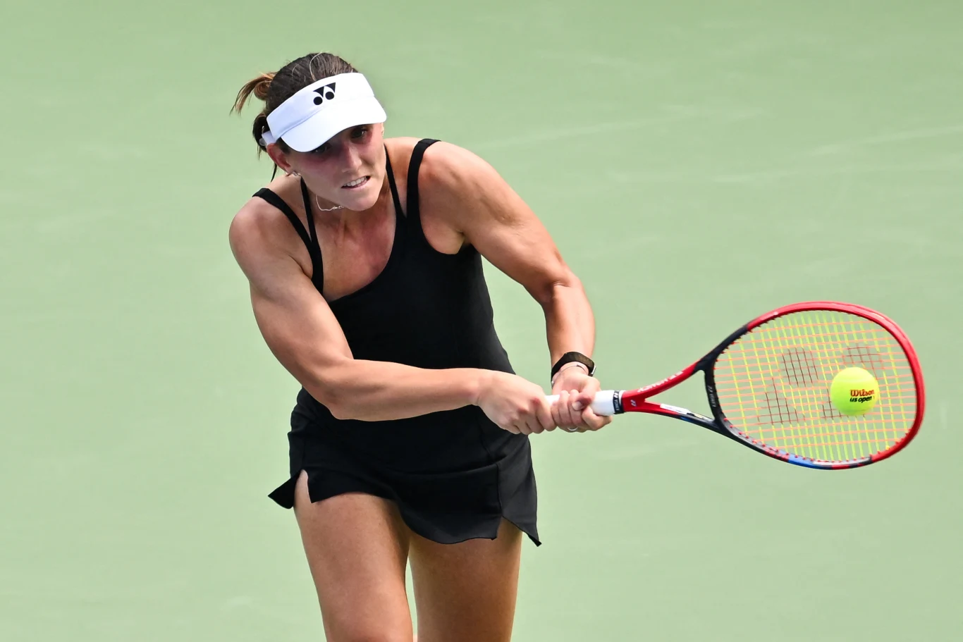 Kobieta w czarnej sportowej sukience i białej czapce odbija piłkę rakietą tenisową na korcie tenisowym podczas gry.