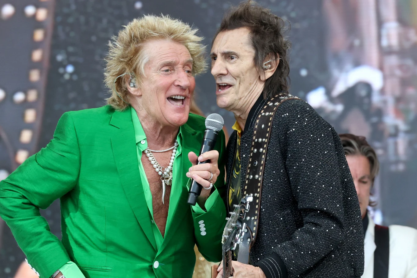 Rod Stewart i Ronnie Wood współtworzyli kiedyś formację Faces Dwóch mężczyzn śpiewających wspólnie na scenie, jeden ubrany w zieloną marynarkę trzyma mikrofon, drugi w czarnej błyszczącej kurtce gra na gitarze, w tle widoczny jest perkusista.