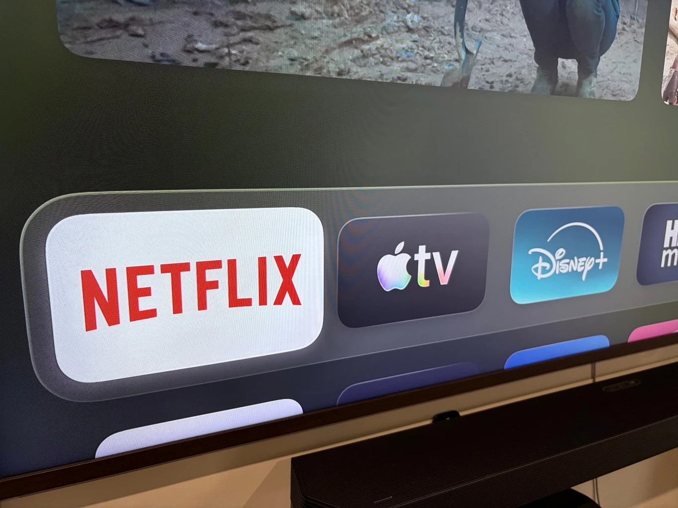 Apple TV+ z nową nazwą. Czas na rebranding. Ekran telewizora z wyraźnie widocznymi ikonami aplikacji streamingowych takich jak Netflix, Apple TV oraz Disney+, na dolnym pasku menu.