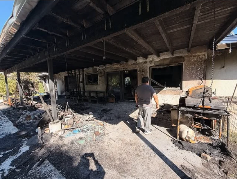 Spalony dom Ramireza Mężczyzna stoi na zniszczonym przez pożar tarasie domu, wokół widoczne są spalone przedmioty, osmalone ściany budynku oraz porozrzucane resztki ze zgliszcz, po prawej stronie znajduje się grill i pies w kagańcu odpoczywający obok spalonego wyposażenia