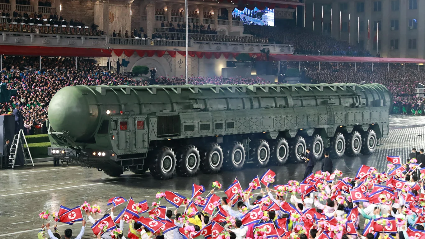 Mobilna wyrzutnia pocisku Hwasong-20. Korea Północna prowadzi politykę regularnego zastrzaszania swoimi możliwościami nuklearnymi, co wpływa na politykę Korei Południowej Potężna wyrzutnia rakietowa na wielu osiach podczas oficjalnej defilady, otoczona przez tłum wiwatujących ludzi trzymających flagi Korei Północnej w gęsto oświetlonym, miejskim otoczeniu.