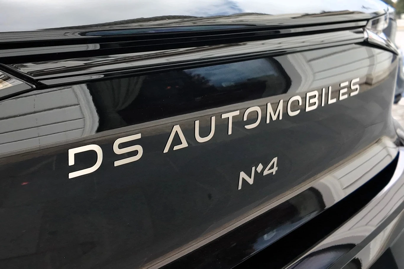Logo DS Automobiles oraz napis N°4 na błyszczącej, czarnej karoserii samochodu, odbijającej fragment budynku.