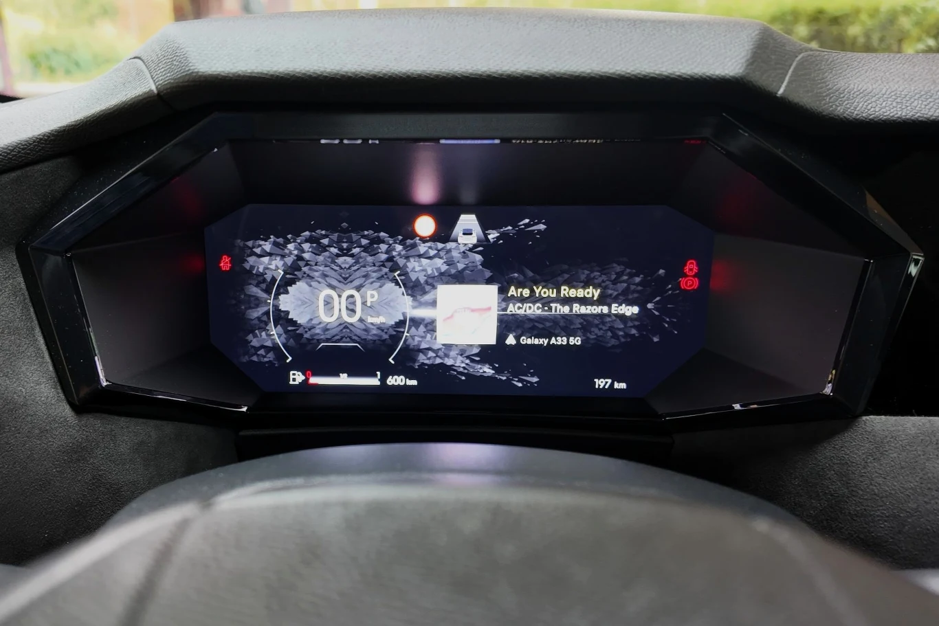 Cyfrowy panel zegarów w samochodzie wyświetla informacje na temat prędkości, zasięgu, orientacji oraz aktualnie odtwarzanej muzyki, w tym tytuł utworu i powiązane urządzenie.