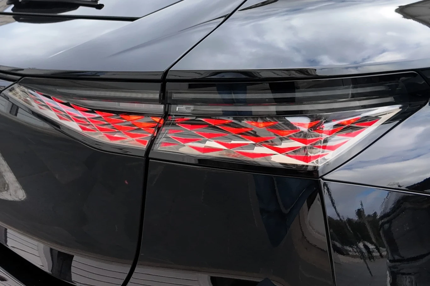 Nowoczesna tylna lampa LED z geometrycznym wzorem w odcieniach czerwieni na błyszczącej czarnej karoserii auta.
