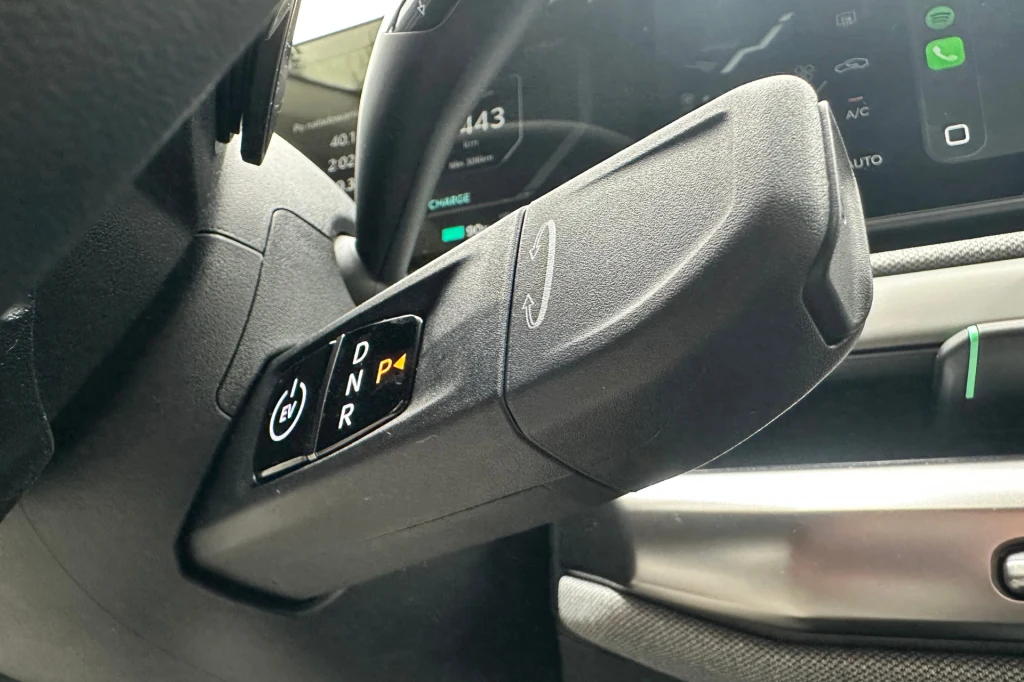 Manetka jest prosta w obsłudze. Co ciekawe, jest podświetlana. Dźwignia zmiany biegów w samochodzie elektrycznym z wyraźnie widocznymi oznaczeniami trybów jazdy, część cyfrowego kokpitu z czytelnym wyświetlaczem oraz fragment kierownicy.