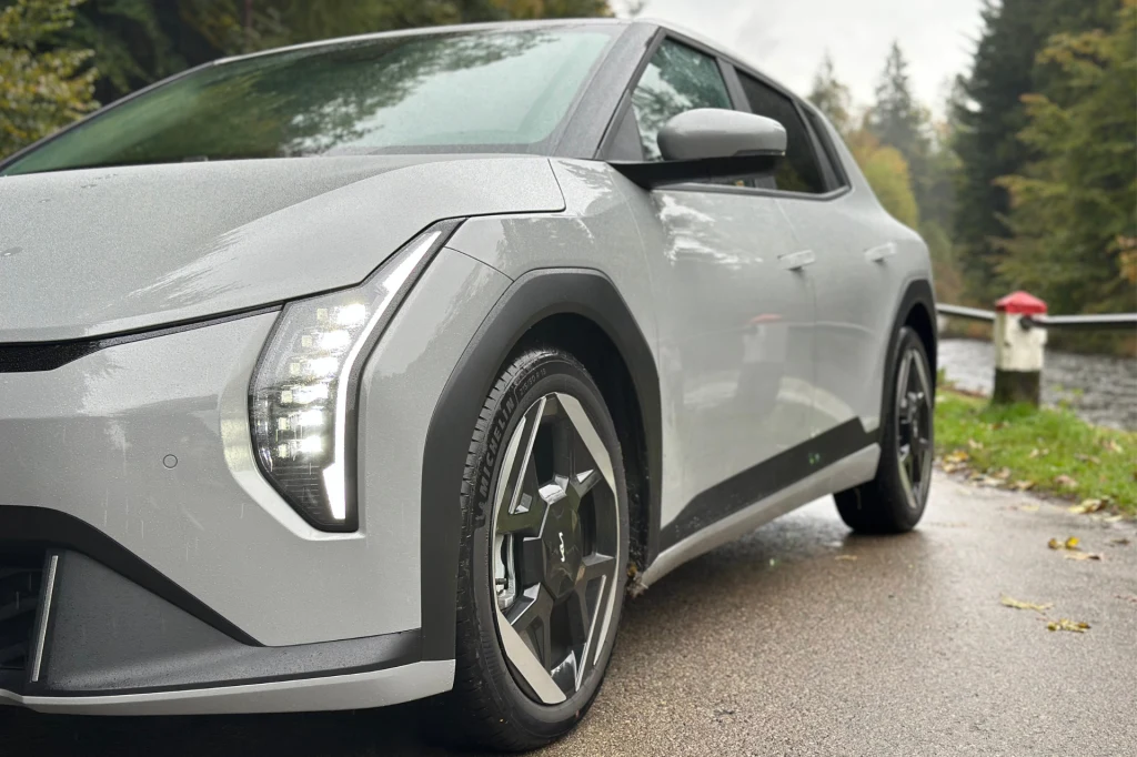 Klamki zostały ukryte - wielu twierdzi, że nie jest to najbardziej użyteczne rozwiązanie, jednakże w tym przypadku chodziło o aerodynamikę Nowoczesny szary samochód elektryczny zaparkowany na wilgotnej drodze w otoczeniu leśnego krajobrazu, z widocznym nowoczesnym oświetleniem LED i sportowymi felgami