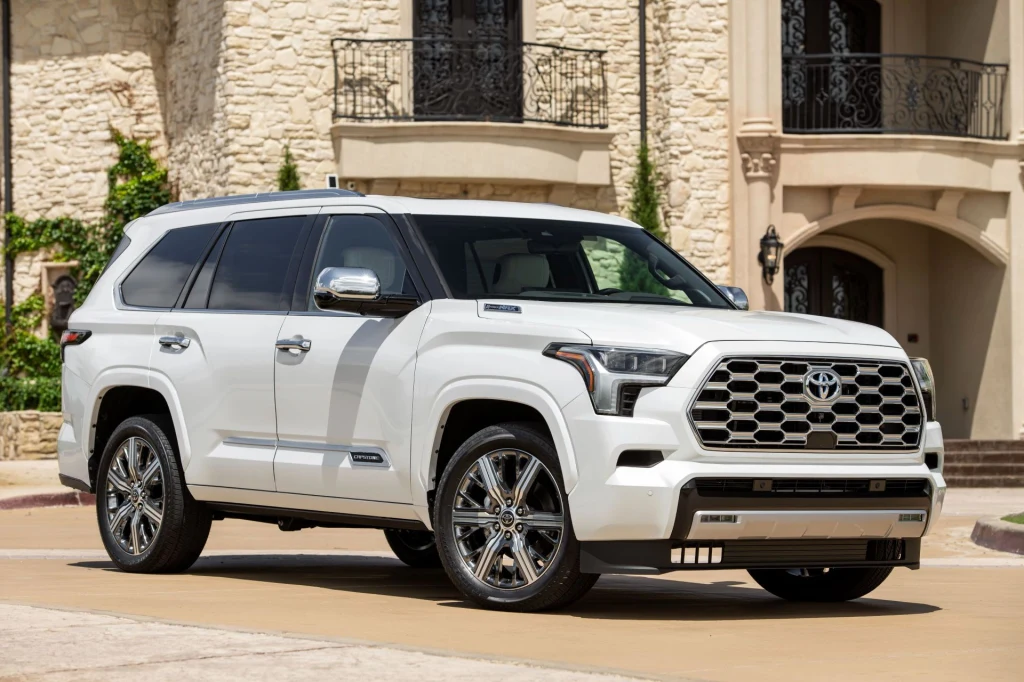 Biały SUV marki Toyota zaparkowany przy stylowym, jasnym budynku o kamiennej elewacji, widoczne chromowane felgi i elementy dekoracyjne pojazdu.