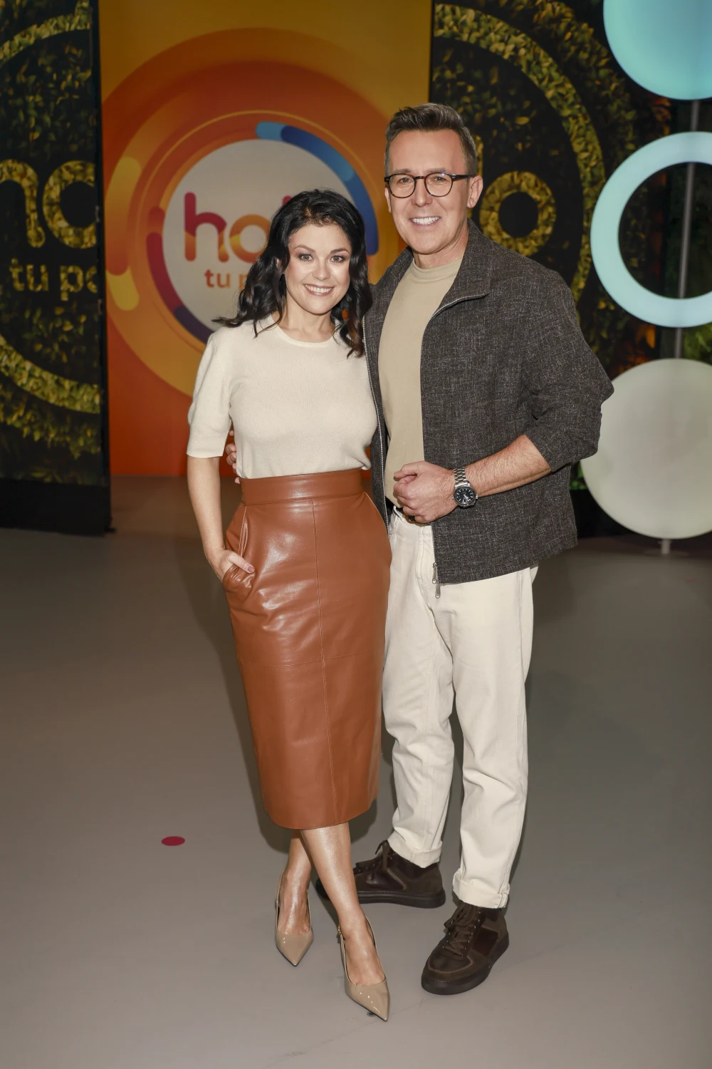 Katarzyna Cichopek w skórzanej spódnicy midi Dwie osoby stoją obok siebie na tle kolorowej ścianki z napisem programu telewizyjnego, ubrane w eleganckie, codzienne stroje, oboje uśmiechnięci, prezentują się w przyjaznej i oficjalnej atmosferze.