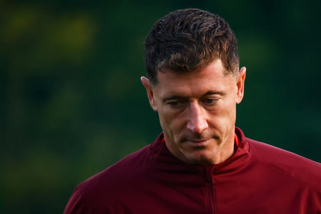 Robert Lewandowski Mężczyzna w bordowej bluzie z opuszczoną głową na tle zieleni, wyrażający skupienie lub zadumę