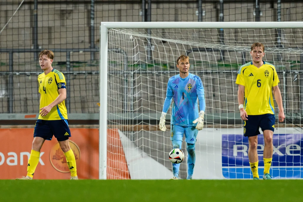 Trzech piłkarzy drużyny Szwecji na boisku podczas meczu piłki nożnej, dwóch ubranych w żółte stroje z numerami, trzeci w stroju bramkarza, za nimi bramka z siatką.