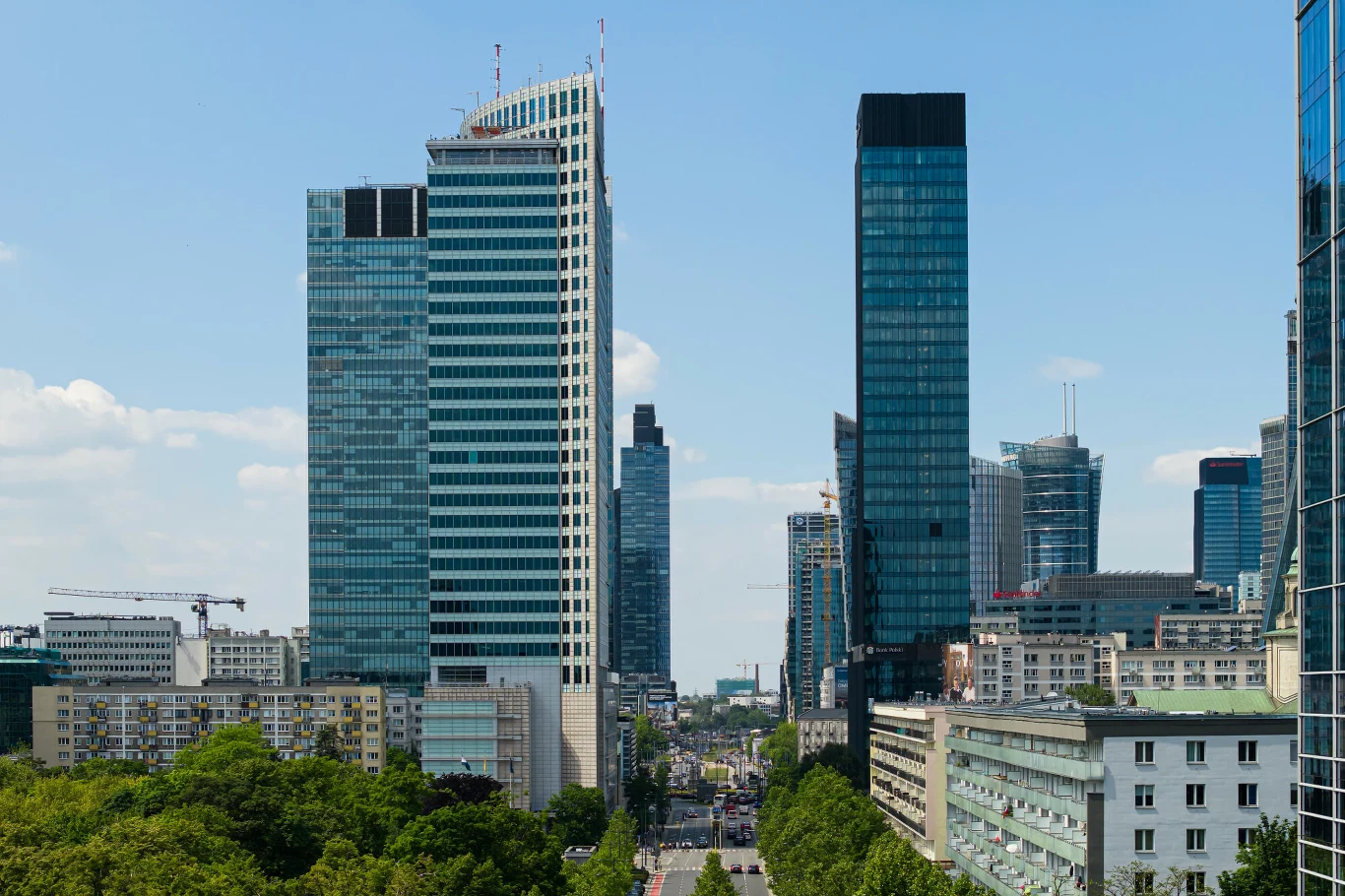 Brytyjski dziennik "The Times" chwali tempo polskiego rozwoju gospodarczego Nowoczesne wieżowce dominujące nad miejską ulicą, otoczone zielenią drzew, z widoczną jasną zabudową i błękitnym niebem w tle.