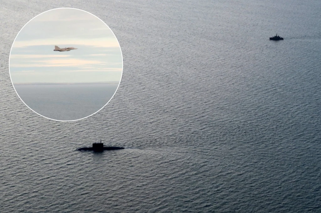 Na morzu widoczny okręt podwodny oraz okręt nawodny, zbliżenie pokazuje dodatkowo przelatujący myśliwiec wojskowy.