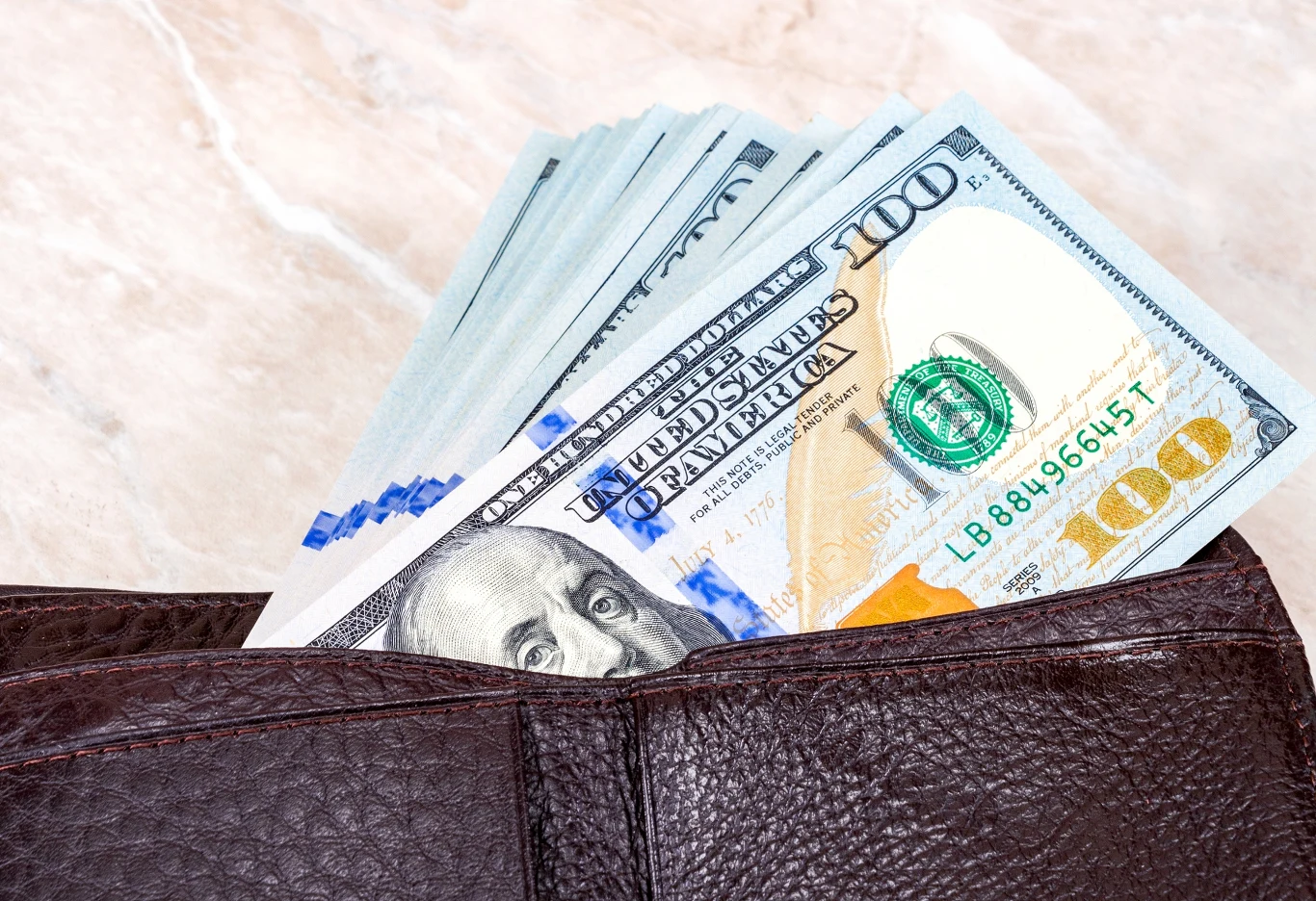 Dolar kosztuje 3,64 zł Brązowy portfel wykonany ze skóry, z którego wystaje kilka banknotów studolarowych, jasno widoczny nominał i fragment wizerunku amerykańskiego prezydenta.