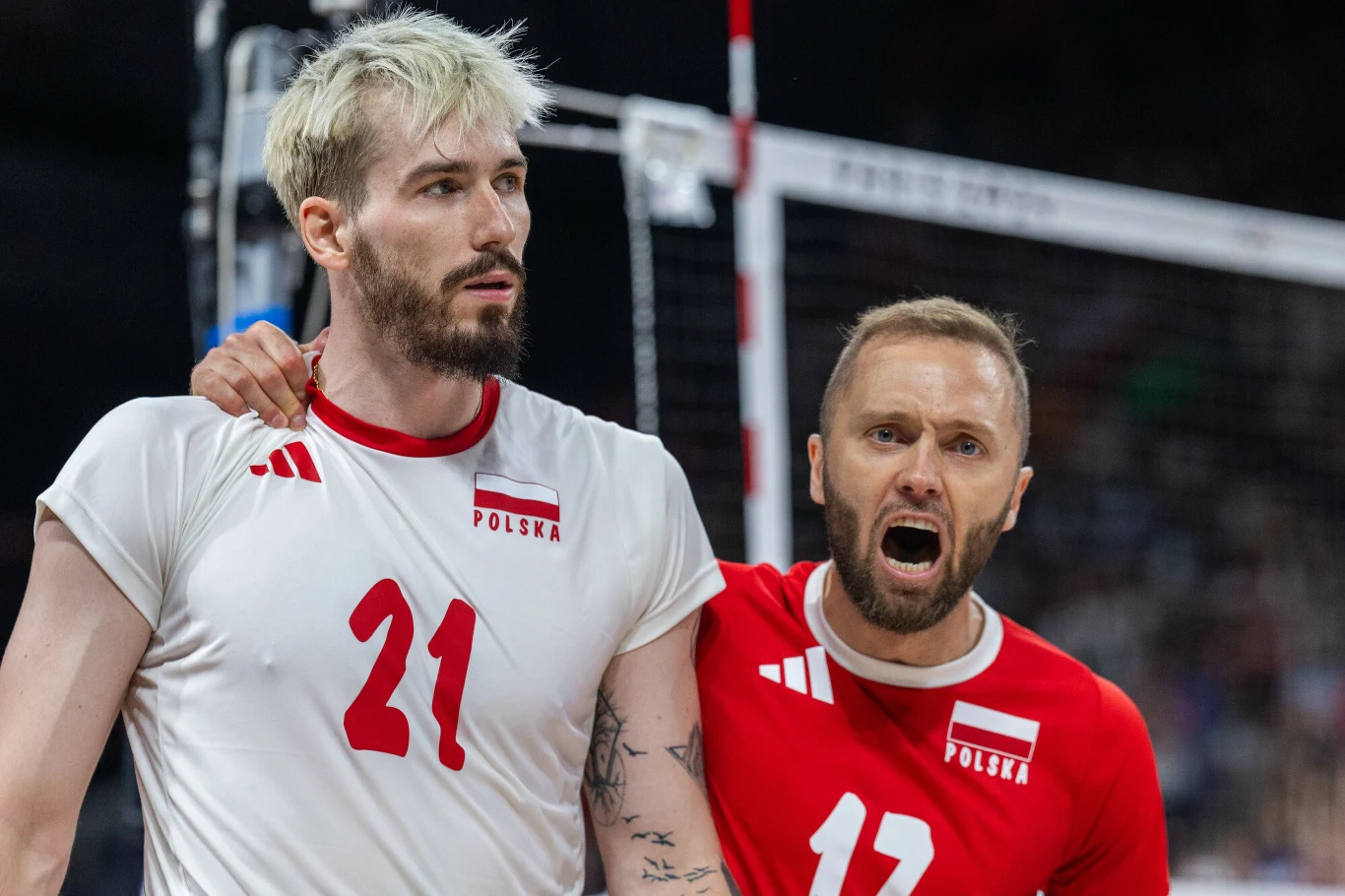 Dwóch siatkarzy reprezentacji Polski w emocjonującym momencie meczu, jeden obejmuje drugiego, obaj noszą stroje sportowe z nazwą kraju i numerami.