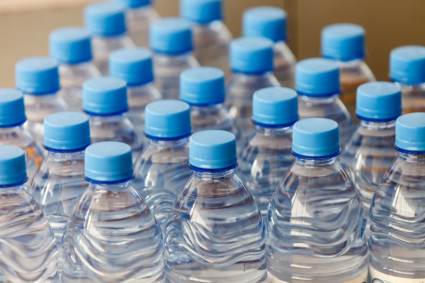 Partia wody Primavera wycofana ze sprzedaży w Auchan (zdj. ilustracyjne) Rzędy plastikowych butelek z wodą mineralną, zakręconych niebieskimi nakrętkami, ustawione blisko siebie, tworząc powtarzalny wzór.