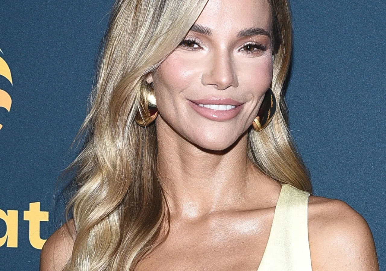 Maja Bohosiewicz Kobieta z długimi, falowanymi blond włosami, uśmiechnięta, ubrana w jasny top, widoczna na tle z elementem graficznym i literami.