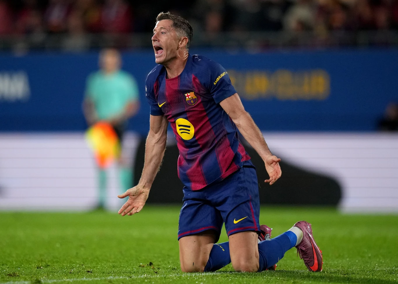 Robert Lewandowski Piłkarz w stroju klubu FC Barcelona klęczy na murawie boiska, z wyrazem emocji i wzniesionymi ramionami, prawdopodobnie podczas meczu piłkarskiego.