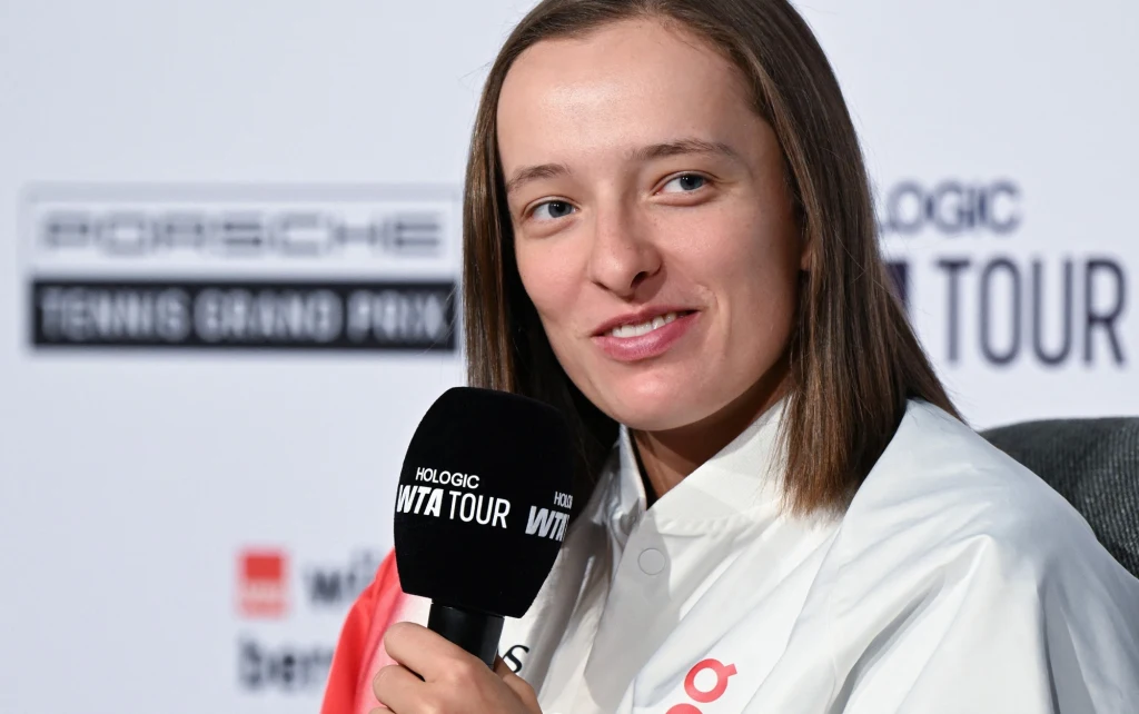 Iga Świątek Młoda kobieta uśmiecha się i trzyma mikrofon podczas konferencji prasowej na tle banerów turnieju tenisowego