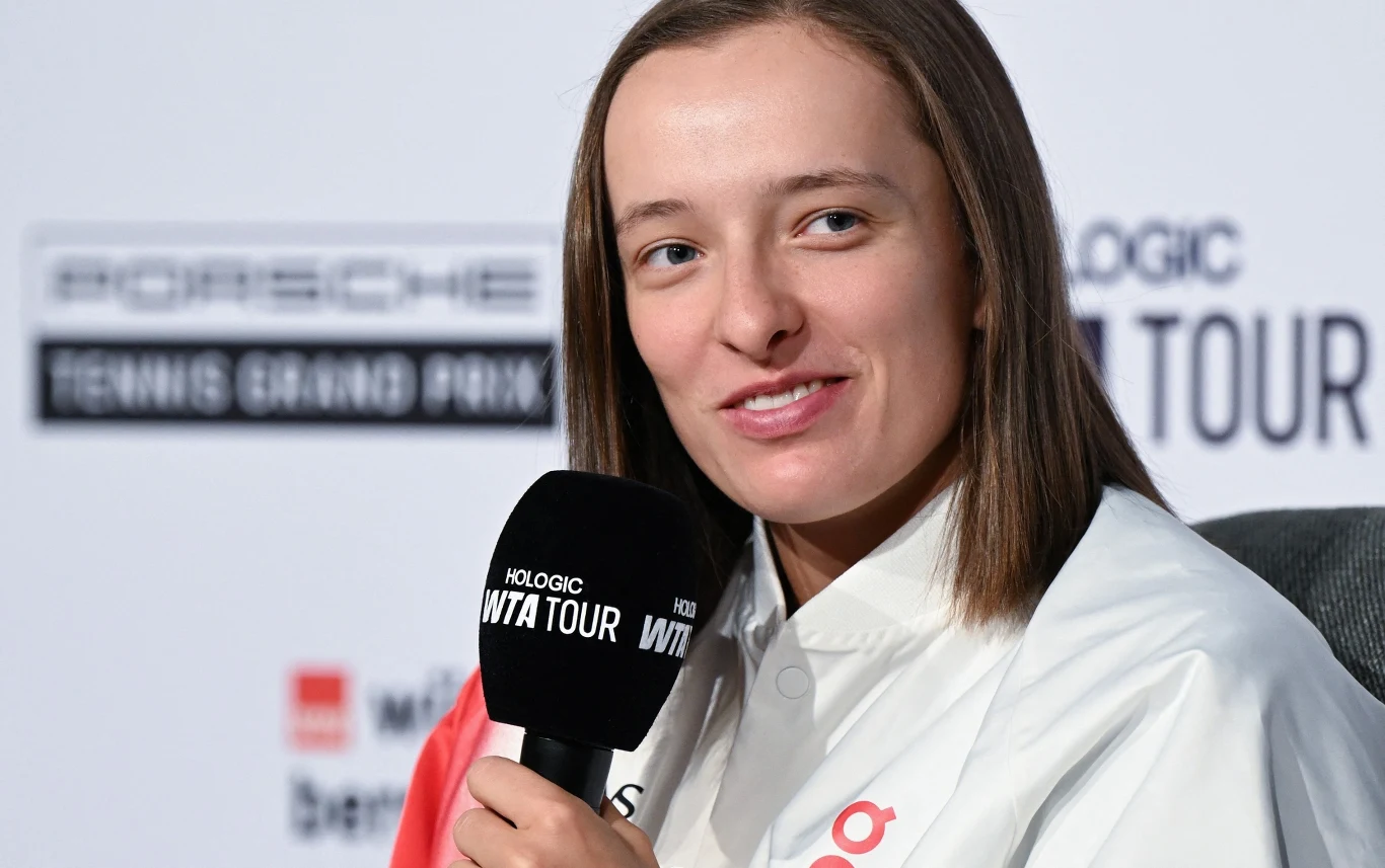 Iga Świątek Młoda kobieta uśmiecha się i trzyma mikrofon podczas konferencji prasowej na tle banerów turnieju tenisowego
