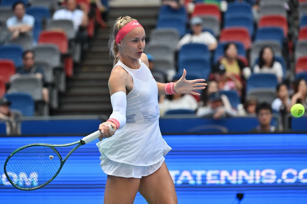 Sramkova w ćwierćfinale w Osace Tenisistka w białym stroju uderza piłkę podczas meczu na profesjonalnym korcie, w tle widownia zajmująca kolorowe siedzenia.