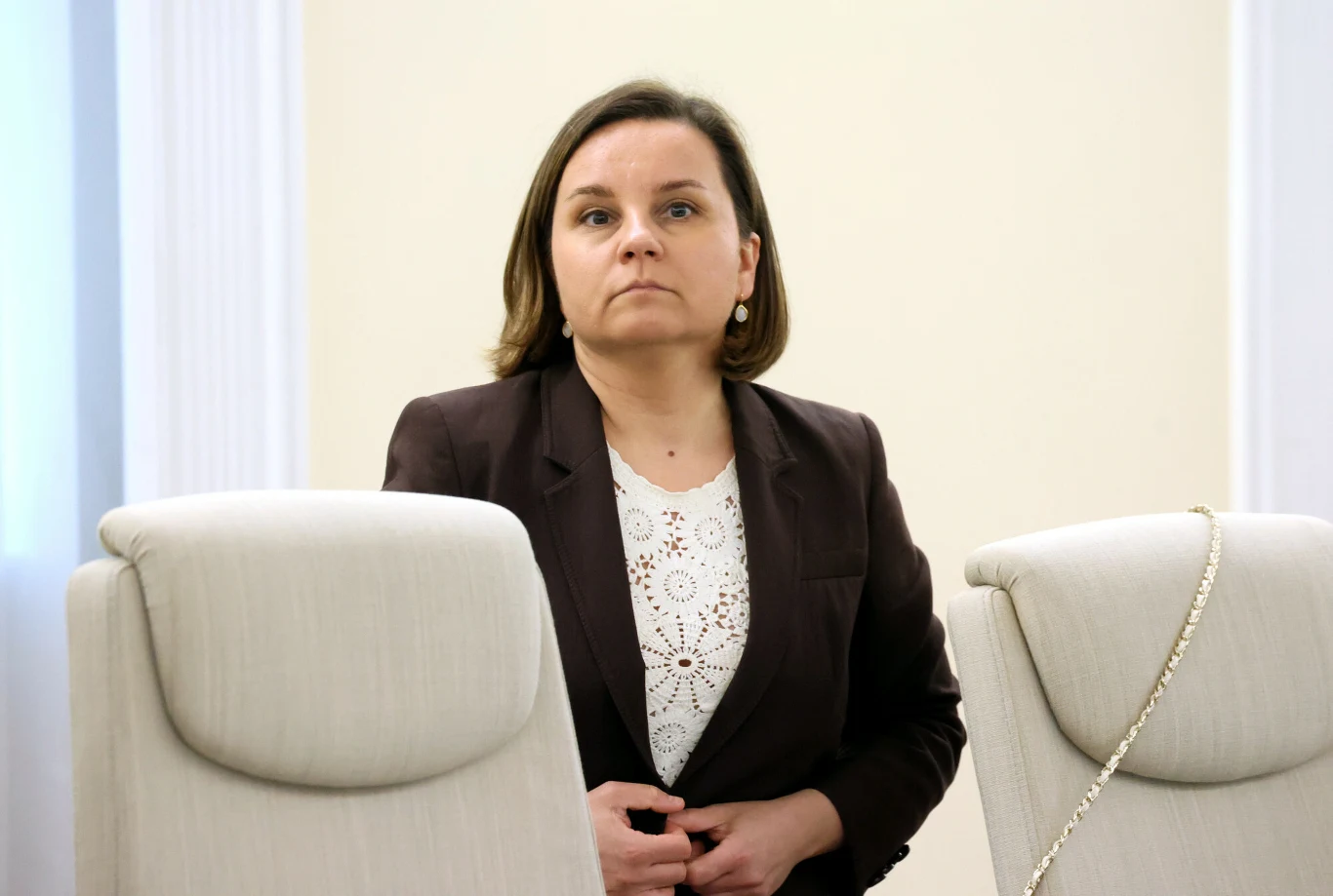 Wiceminister klimatu i środowiska Urszula Zielińska Kobieta w ciemnej marynarce i jasnej bluzce stoi między dwoma kremowymi krzesłami w jasnym, minimalistycznym wnętrzu.