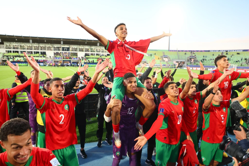 Maroko - Francja, półfinał MŚ U-20 2025 Piłkarze w czerwono-zielonych strojach świętują sukces na boisku, jeden z nich siedzi na ramionach kolegi, wszyscy mają rozłożone ręce w geście triumfu, w tle stadion i publiczność.