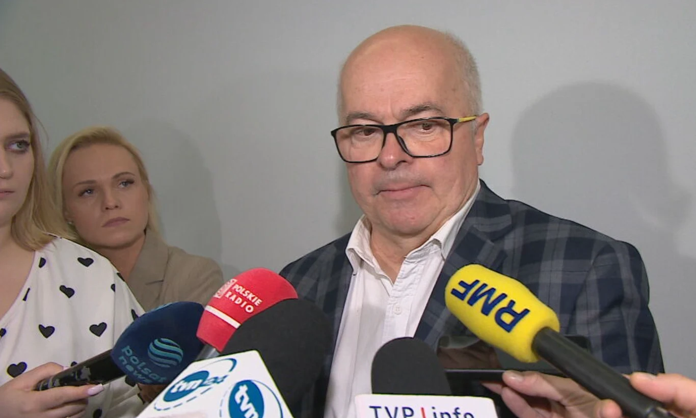 Poseł Tomasz Zimoch Mężczyzna w okularach i marynarce stoi w otoczeniu dziennikarzy z mikrofonami różnych stacji telewizyjnych, w tle dwie kobiety słuchające wypowiedzi.