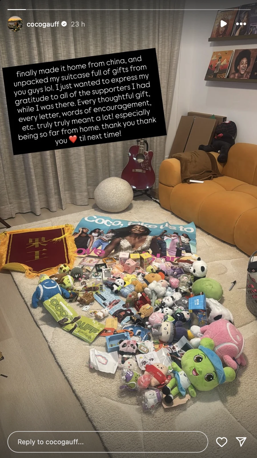 Duża ilość różnorodnych pluszaków, maskotek, kart i prezentów rozłożonych na dywanie w salonie obok rozkładanego plakatu sportowego, w tle jasna kanapa oraz osobiste zdjęcia na półce.