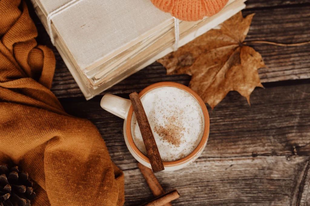 Syrop możemy dodać bezpośrednio do filiżanki lub korzystając z funkcji Sweet Foam, połączyć go z mleczną pianką Kubek kawy lub gorącej czekolady z pianką i cynamonem, obok leżące stare książki, suchy liść klonu oraz ciepły, pomarańczowy sweter, całość utrzymana w jesiennej, przytulnej stylistyce.