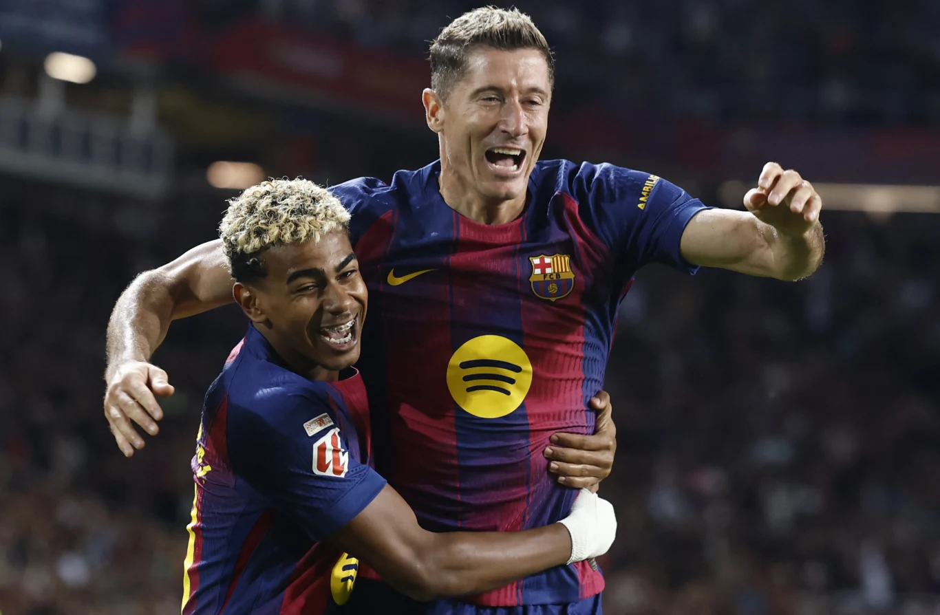 Dwóch piłkarzy Barcelony w granatowo-bordowych koszulkach obejmuje się i świętuje sukces na tle stadionu, na twarzach widoczna radość i emocje.
