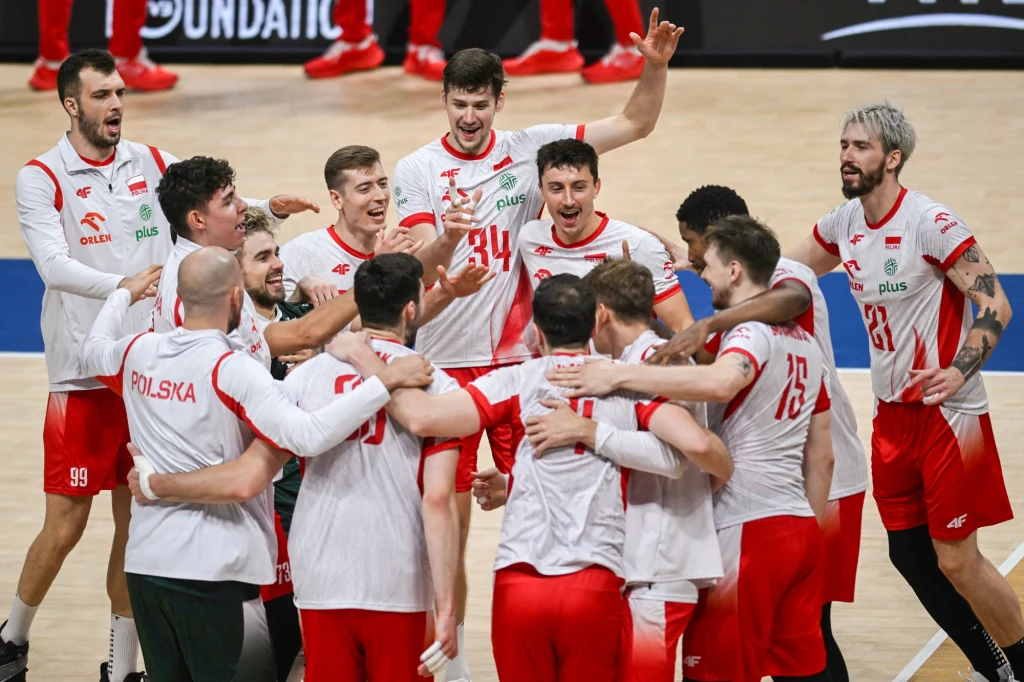 Polscy siatkarze w białych i czerwonych strojach zgromadzeni w kręgu na parkiecie, wyrażają radość i entuzjazm, przytulają się oraz świętują wygraną.