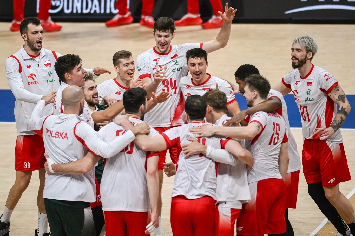 Siatkarze reprezentacji Polski świętujący zdobycie brązu na mistrzostwach świata Polscy siatkarze w białych i czerwonych strojach zgromadzeni w kręgu na parkiecie, wyrażają radość i entuzjazm, przytulają się oraz świętują wygraną.