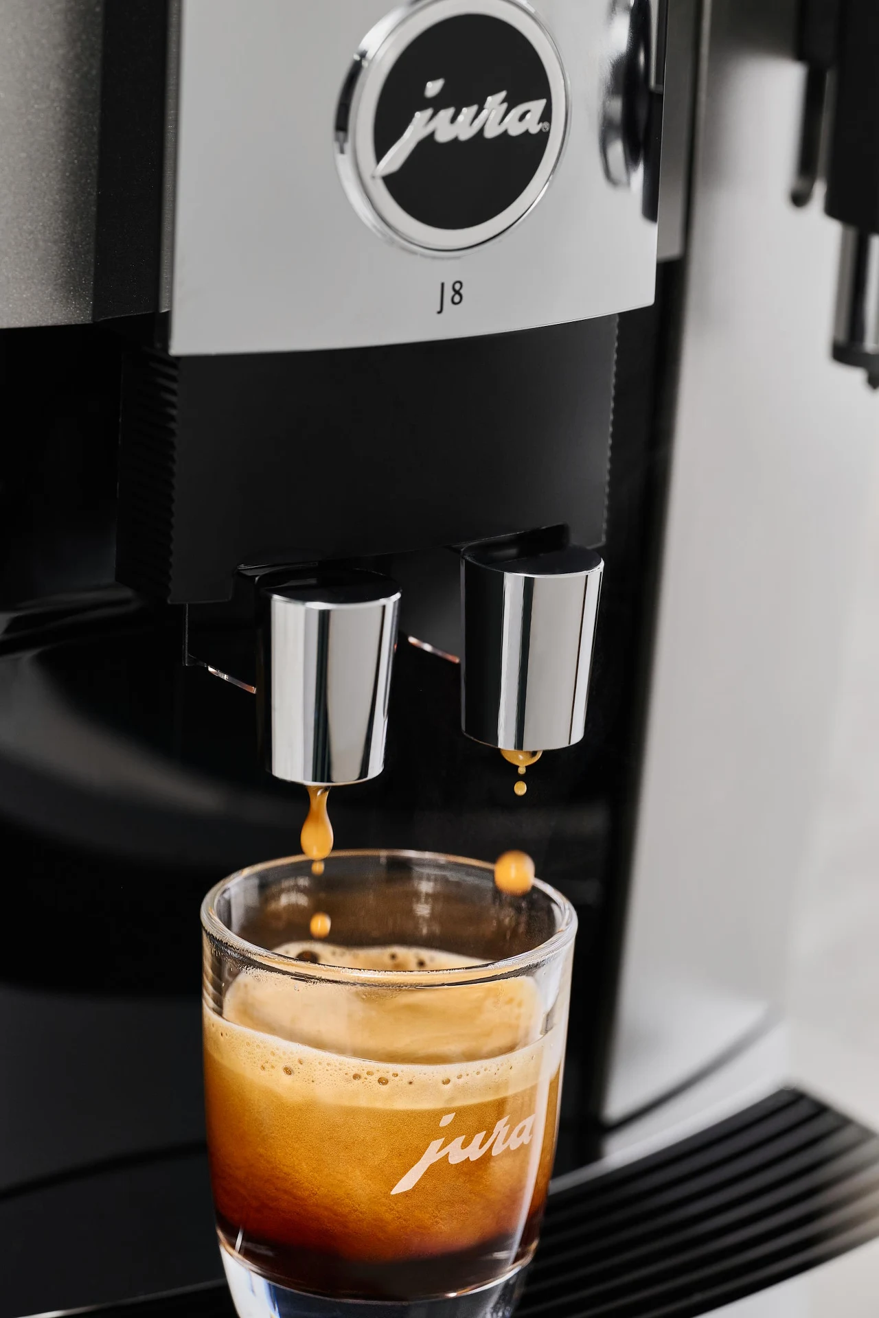 Smak kawy często mówi więcej o kondycji ekspresu niż o... samej kawie Ekspres do kawy marki Jura przygotowujący świeże espresso, spływające do szklanej filiżanki z widoczną warstwą gęstej cremy.