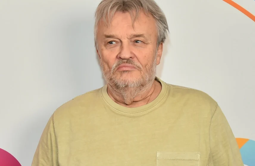 Krzysztof Cugowski zdradził, że ma już spisany testament Starszy mężczyzna z siwymi włosami i zarostem, ubrany w jasną koszulkę, patrzy na bok na tle jasnej ściany z kolorowymi elementami graficznymi.