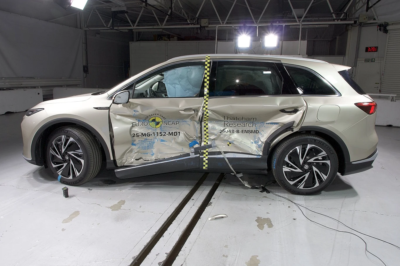 SUV po testach zderzeniowych z widocznymi uszkodzeniami bocznymi, oznaczeniami instytutu badawczego oraz specjalistycznymi znacznikami na drzwiach, całość otoczona laboratoryjnym oświetleniem.