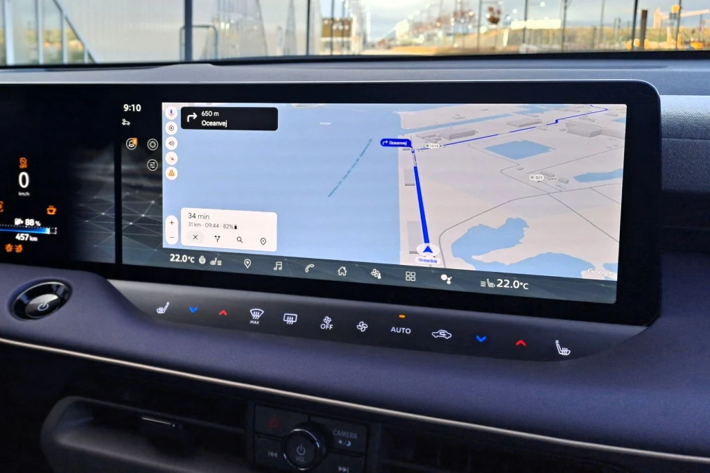 System multimediów Nissana Leafa wyposażony jest we wbudowane usługi Google. Dzięki temu mamy np. dostęp do Map Google bez łączenia się z telefonem. Duży ekran dotykowy samochodu z włączoną nawigacją, mapa wyznaczająca trasę przejazdu przez most lub drogę biegnącą nad wodą, na dole widoczne przyciski sterujące klimatyzacją oraz podstawowe funkcje pojazdu.