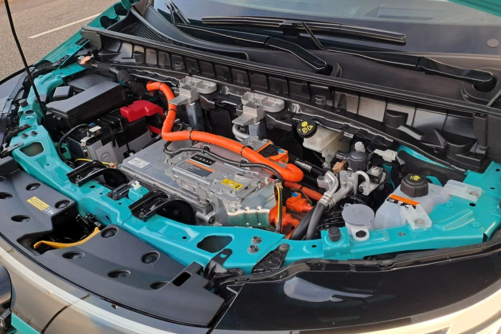 Nissan Leaf dostępny jest w dwóch wariantach mocy: 177 KM i 218 KM. Silnik samochodu elektrycznego z wyeksponowanymi elementami instalacji wysokiego napięcia, widocznymi pomarańczowymi przewodami oraz innymi podzespołami technicznymi pod maską.