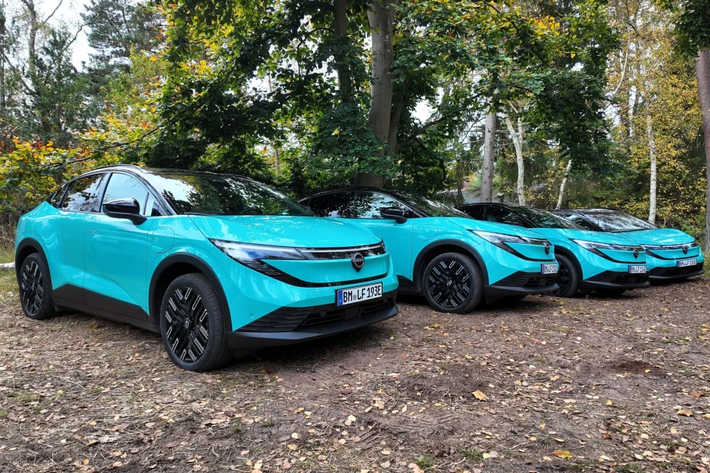 Nissan Leaf pojawić się ma w naszym kraju wiosną 2026 roku. Trzy nowoczesne samochody marki Opel w intensywnie turkusowym kolorze zaparkowane na tle lasu, dominują drzewa z zielonymi i żółtymi liśćmi oraz naturalne leśne podłoże.