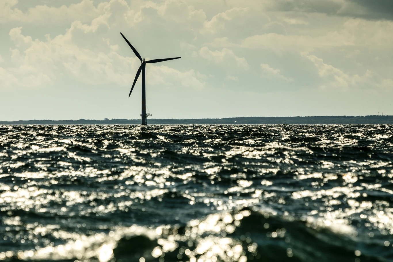 Senat jednogłośnie przyjął ustawę o morskiej energetyce wiatrowej Pojedyncza turbina wiatrowa stojąca na otwartym morzu, błyszcząca powierzchnia wody odbijająca światło, rozległe niebo z chmurami w tle.