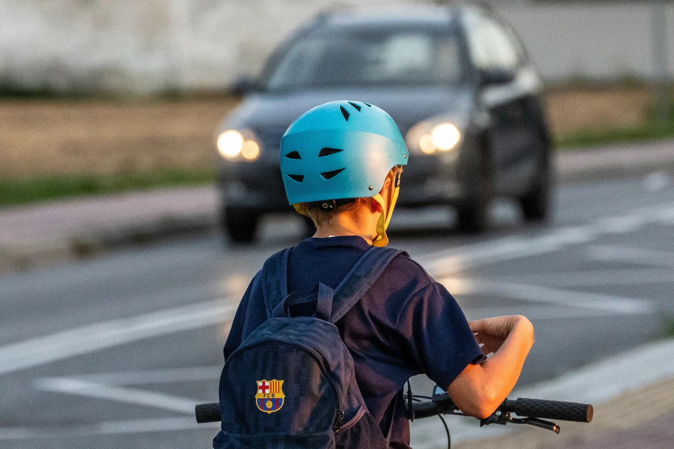 Od 3 czerwca 2026 r. dzieci poniżej 16. roku życia muszą jeździć e-hulajnogą w kasku ochronnym. Chłopiec w niebieskim kasku rowerowym i plecaku jadący hulajnogą po drodze, w tle samochód jadący po tej samej ulicy.