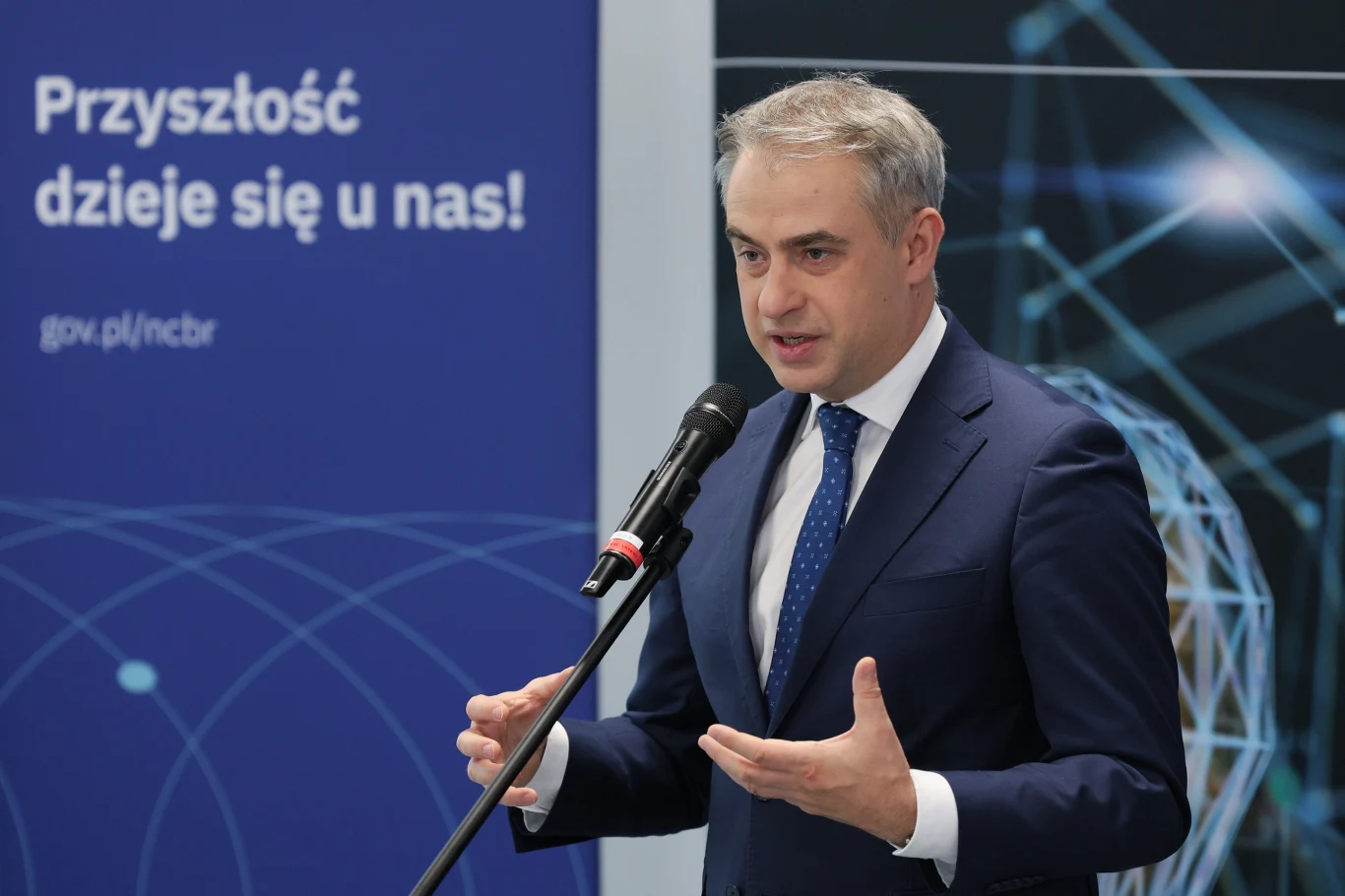 Polska stawia na rozwój sztucznej inteligencji i technologii kwantowych - mówił wicepremier i minister cyfryzacji Krzysztof Gawkowski podczas prezentacji unijnego programu STEP Mężczyzna w garniturze przemawia do mikrofonu na tle nowoczesnej, technologicznej grafiki oraz tablicy z napisem 'Przyszłość dzieje się u nas!'