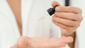 Ręce osoby aplikującej krople lub olejek z pipety na otwartą dłoń, ujęcie skupione na dłoniach i akcesorium kosmetycznym.