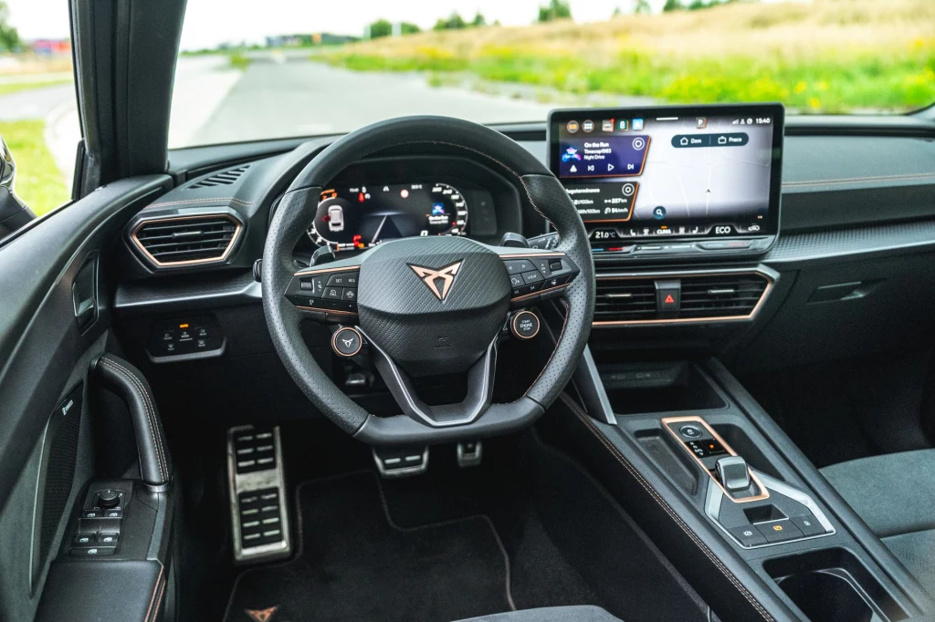 Cupra zaktualizowała usługi cyfrowe, pojawił się nowy interfejs wskaźników i system multimediów. Kokpit nowoczesnego samochodu marki Cupra z cyfrowym zestawem wskaźników, multifunkcyjną kierownicą i dużym wyświetlaczem dotykowym na konsoli centralnej, widoczne sportowe wykończenie i elektroniczne detale.