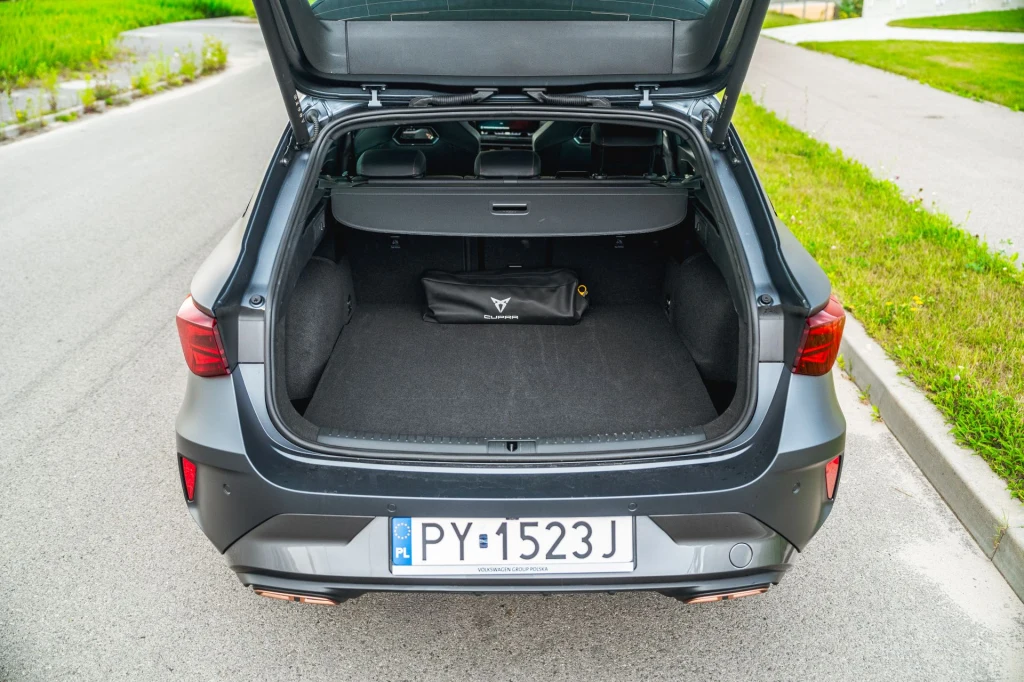 Bagażnik Cupry Leon Sportstourer z hybrydą plug-in pomieści 470 litrów. Otwarty bagażnik ciemnoszarego samochodu zaparkowanego na ulicy, z widoczną czarną torbą w środku i tablicą rejestracyjną PY 1523J.