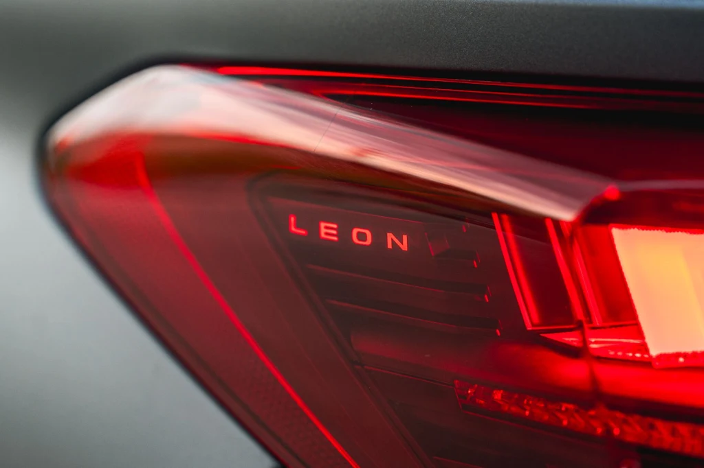 Po modernizacji światła tylne Cupry Leon zostały wyposażone w zmienną sygnaturę. Zbliżenie na tylną lampę samochodu marki SEAT Leon, widoczny napis LEON na przezroczystej części lampy, dominująca czerwień świateł.